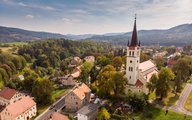 Kościół z wysoką wieżą wśród zabudowy miasteczka i zielonych wzgórz