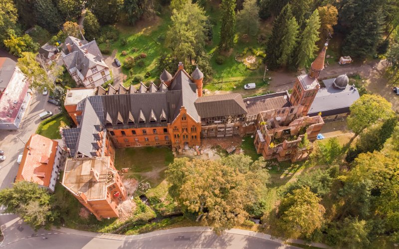 Zabytkowy kompleks budynków otoczony parkiem widziany z lotu ptaka