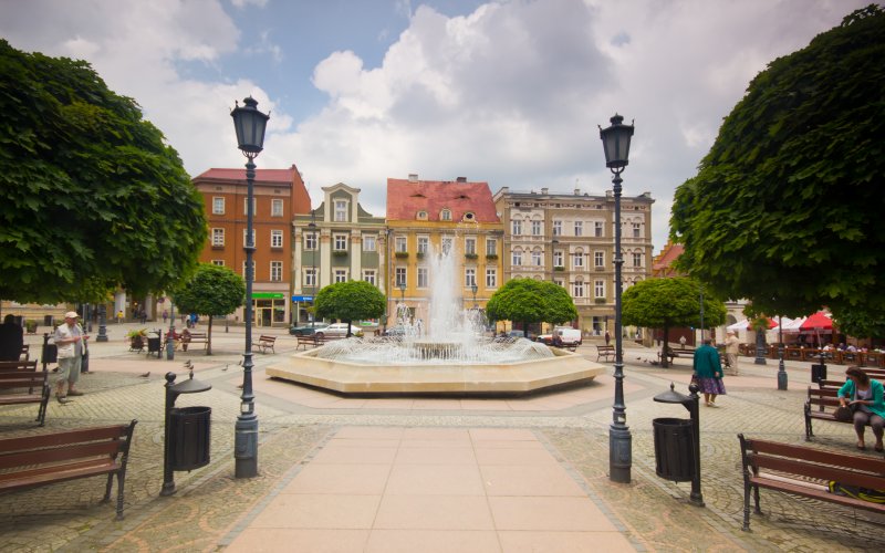 Plac miejski z fontanną i pastelowymi kamienicami w otoczeniu latarni