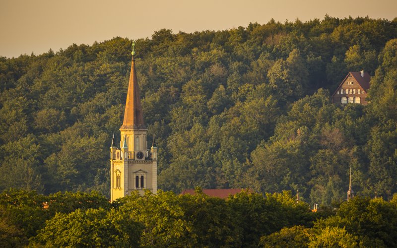 Kościół z wysoką wieżą pośród zielonych wzgórz i lasów