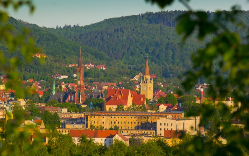 Panorama miasta z kamienicami i wieżą kościoła na tle zielonych wzgórz