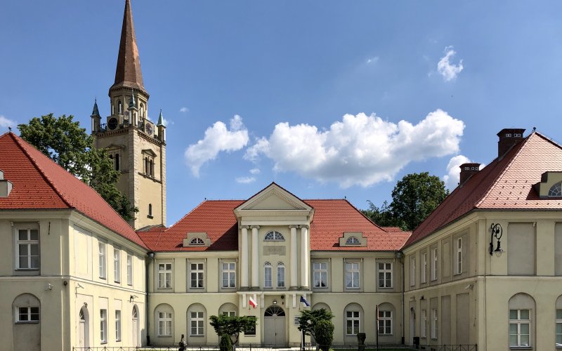 Pałacowy budynek z kolumnami i wieżą kościoła w tle